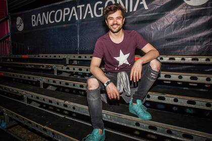 Felipe Colombo, sonriente con ripped jeans, zapas turquesas, buzo a la cintura y remera con estrella en el festival BUE