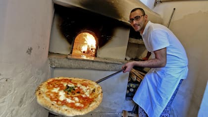 Un hombre muestra una pizza cocinada en el primer horno de piedra que se utilizó en 1889 para hacer la primera pizza margarita en Nápoles, Italia