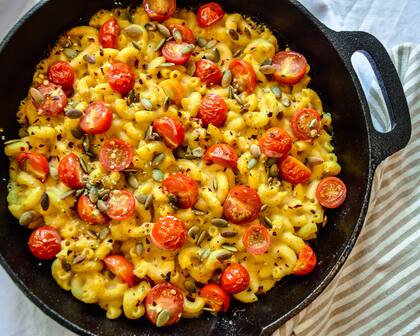 Fideos y queso cremoso fundido, tomates cherry en rodajas, semillas nutritivas de cáñamo, salpicaduras de pimienta roja picante para una cena en casa