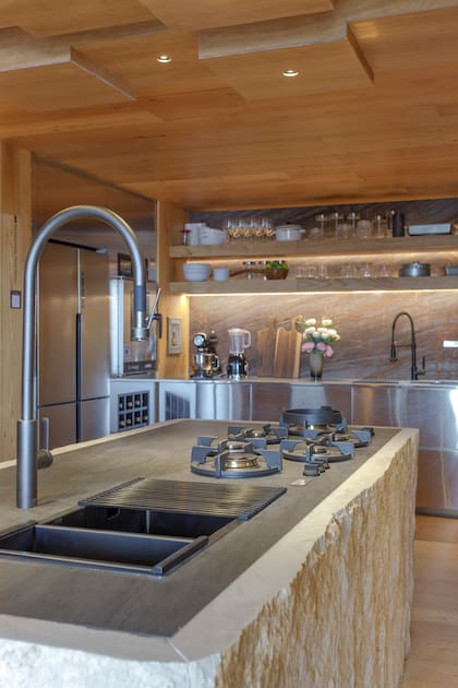 Barra revestida en Neolith 'Basalt Black' con hornallas modelo PITT Cooking (todo de De Stefano). Heladera (Drean). Horno gastronómico (Baires Cocina). Cava con vinos de Gamboa integrada al mobiliario.