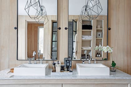 En el baño principal, sectores idénticos para los dueños de casa. Los espejos están colgados de forma tradicional, pero sumaron dos agarres de hierro como detalles deco. Uno similar eligió para las lámparas de noche.