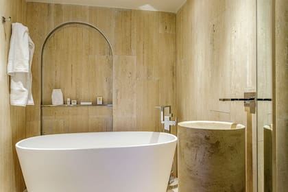 Revestimiento en marmetas de Travertino natural (De Stefano por Mármoles Milán) y tótem en el mismo material con grifería monocomando de pared 'Dominic New' Cromo (FV). Bañadera exenta (Ferrum) con grifería de pie (Novum).