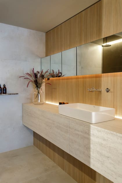 Mesada en Purastone Travertino Navona (De Stefano, Paprika Estudio y Marmolería United Stone). Revestimiento de pared en melamina Camellia especial para humedad (Faplac y Paprika Estudio). Grifería 'Epuyén Bi Comando' (FV). Bacha 'Country baja II' (Ferrum). Garganta de iluminación con perfil Abo (Idea Iluminación).