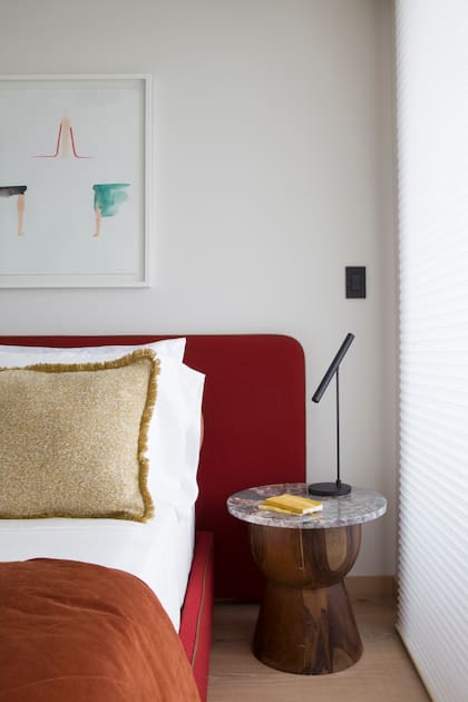 La lámpara "Wipi" de Idea "simboliza la síntesis pura". Mesa redonda de madera maciza con tapa de mármol veteado. Cama en pana bordó y obra de arte con acuarelas enmarcadas.