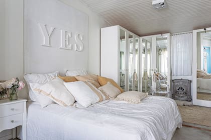 Entre los placares, un tiro balanceado con carcasa de salamandra antigua. Vestida con géneros naturales (Indias Argentina), la cama está coronada por el cuadro ‘Yes’, parte de “Palabras mágicas”, la línea de deco que Carolina hizo hace unos.