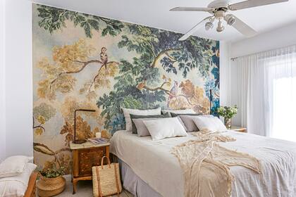 Mural (Anthropologie). Cubreedredón de lino y almohadones (todo, En Abundancia Deco).Velador de acero ‘Steel’ (Rodina Iluminación) y, sobre la consola ‘Cabinet’ de teca (Wood Market), cuadros (Tienda Canvas) y candelabro de madera (Sol Palou Deco).