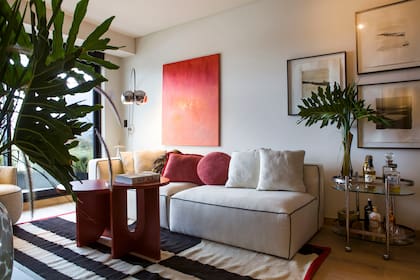 Sillón grande tapizado en lino grueso 100% off white con vivo en lino negro y base de madera y sillón individual tapizado en lana italiana (Concepto Fusión). Alfombra rayada blanco y negro con vivo colorado. Mesas coffee table laqueadas en colorado (todo de Concepto Fusión).