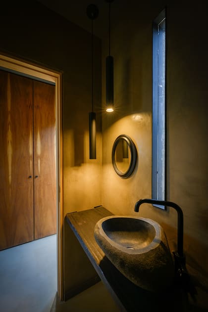 Los colores oscuros le dan al toilette un clima súper íntimo. Su bacha la hizo un artesano local con piedra del río y la abertura permite espiar el exterior.