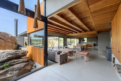En el hall, lámpara colgante de techo en madera y gran ventanal corredizo que da a las enormes piedras.