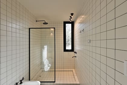 Las arquitectas quisieron darle a cada baño una identidad diferente. Este es el más claro, con azulejos en blanco que contrastan con detalles en negro, como la grifería, los spots o la pastina.