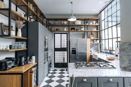 A la izquierda, un mueble esconde una pileta de lavar y una mesa rebatible para el planchado. Anafe (Smeg), bacha de losa semiencastrada ‘Country’ (Ferrum), grifería ‘Cento Semi-Pro’ (Hansgrohe), estantería de hierro y petiribí (Rob Ortiz).