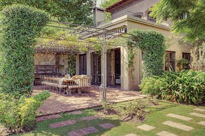 Bajo la pérgola de hierro se ubicó la mesa con tapa de durmientes de pino tea (Amighini). Sillas y sillones de hierro (Bielfer). Los pisos son de ladrillones de Córdoba.