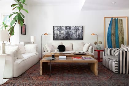 Foto en blanco y negro de Ezequiel Rohr y, parado, cuadro de Carlos Taquini. Sillón con funda rayada (Hermanas Caradonti). Mesita laqueada en rojo modelo ‘Cilindro’ (Nisla Estudio). Alfombra (Casa Sixta). Mesas ratonas en pergamino (Harturo)