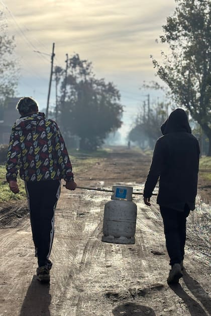 Foto registrada por @ailinbasualdo donde se ve a dos jóvenes unidos por una rama con la que se ayudan para cargar una garrafa
