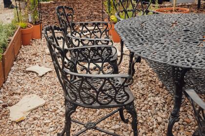 Para compartir comidas y sobremesas, un juego de comedor en hierro forjado negro, con respaldo ornamentado y asiento calado.