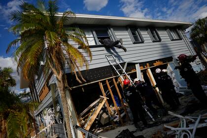 Los miembros de Florida Task Force 2 de búsqueda y rescate urbano obtienen acceso a una casa a través de una ventana superior rota para confirmar que la casa está libre de personas y restos humanos, una semana después del paso del huracán Ian, en Fort Myers Beach, Florida, el 5 de octubre de 2022