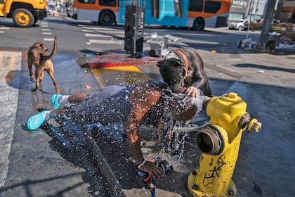 Víctor Tejada y su perro se refrescan con agua de un hidrante en el área de Skid Row de Los Ángeles el 31 de agosto de 2022, en medio de advertencias de calor excesivo