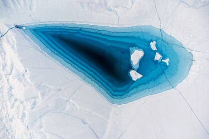 El agua turquesa se ve en un gran agujero de deshielo en la parte superior de un iceberg en la bahía de Disko, Ilulissat, al oeste de Groenlandia. Los icebergs se originan en el glaciar Jakobshavn (Sermeq Kujalleq), el glaciar más productivo del norte del Hemisferio. Los enormes icebergs que se desprenden del glaciar flotan durante años en las aguas frente al fiordo antes de ser arrastrados hacia el sur por las corrientes oceánicas.