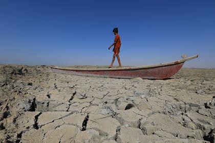 Un niño camina en un bote dejado sobre el lecho seco de una sección de las marismas del sur de Irak de Chibayish, en la provincia de Dhi Qar, el 28 de junio de 2022. - La sequía de Irak refleja una disminución en el nivel de las vías fluviales debido a la falta de lluvia y flujos más bajos de los países vecinos río arriba, Irán y Turquía.