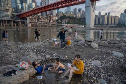 La gente se sienta en un charco de agua en el lecho del río Jialing, un afluente del Yangtze, en la municipalidad de Chongqing, en el suroeste de China, el 20 de agosto de 2022. El paisaje de Chongqing, una megaciudad que también incluye tierras de cultivo circundantes y paisajes pintorescos montañas, ha sido transformado por la sequía.