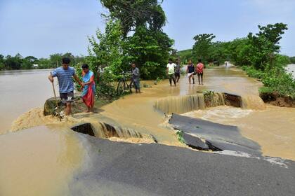 Las personas caminan por una carretera dañada por las aguas de la inundación después de las fuertes lluvias en el distrito de Nagaon, estado de Assam, el 19 de mayo de 2022. - Al menos 10 personas, incluido un niño de cuatro años, han muerto en inundaciones y deslizamientos de tierra después de las inusuales lluvias torrenciales que azotaron la región en la India