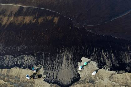 Los trabajadores limpian petróleo de la playa Cavero en Ventanilla, Callao, Perú, el 18 de enero de 2022. El Instituto de Defensa Civil de Perú dijo que la erupción de un volcán submarino en Tonga creó olas altas que movieron un barco que cargaba petróleo en la refinería La Pampilla, causando un gran derrame