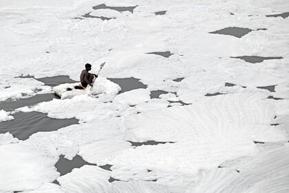 Un hombre rema en su balsa mientras recolecta materiales reciclables en las aguas del río Yamuna cubiertas con espuma contaminada en Nueva Delhi el 5 de julio de 2022.