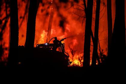  Un bombero rocía agua hacia las llamas en un incendio forestal cerca de Belin-Beliet, suroeste de Francia, el 11 de agosto de 2022. 