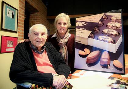 Francisco Bellotti y su hija María Fernanda junto a una antigua publicidad de los bombones Amore, también creados por él
