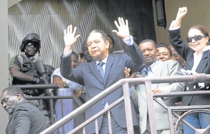 Frente a su hotel, Duvalier saluda a un puñado de seguidores mientras es escoltado por la policía