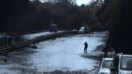 Un hombre camina por una ruta con el barro por las rodillas