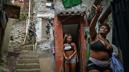 Una mujer cuelga la ropa mientras policías militarizados vigilan en la favela de Rocinha en Río de Janeiro