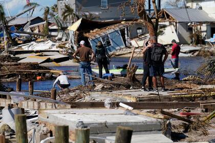Gente de pie en el puente destruido a Pine Island mientras contemplan los daños causados por el huracán Ian en Matlacha, Florida