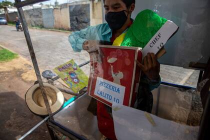 De pie, detrás de la ventana del protector de plástico de su aula móvil, Gerardo Ixcoy sostiene una caja de pizza como parte de una lección sobre fracciones