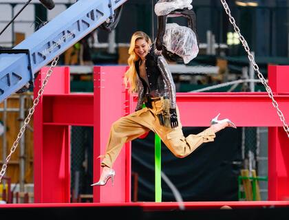 Gigi Hadid es vista en el set de una sesión de fotos para Maybelline en la ciudad de Nueva York. Gigi colgaba de una viga de acero en un patio de construcción mientras vestía un chaleco de mezclilla, un top plateado, guantes negros, pantalones tipo paracaídas y tacones plateados