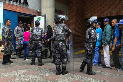 Policías vigilan la entrada de un supermercado en Caracas para evitar saqueos