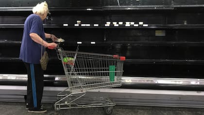 Una mujer toma un queso de cabra de una góndola de quesos casi vacía en un supermercado de Caracas