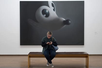 Una visitante se sienta en un banco junto a la pintura "Grey Mouse 4"
