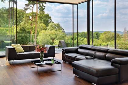 Gracias a los paneles de vidrio corredizos, el living continúa casi ininterrumpidamente en un balcón con barandas de vidrio que parece suspendido sobre el paisaje.