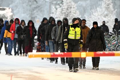 Guardias fronterizos finlandeses escoltan a migrantes en el cruce internacional entre Finlandia y Rusia, en Salla, Finlandia, jueves 23 de noviembre de 2023. (Jussi Nukari/Lehtikuva via AP)