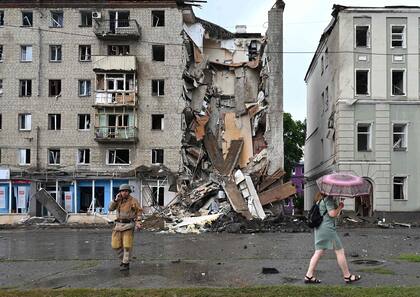 Un residente local pasa junto a un rescatista ucraniano que trabaja fuera de un edificio parcialmente destruido después de un ataque con misiles rusos en Kharkiv el 11 de julio de 2022, en medio de la invasión militar de Rusia lanzada contra Ucrania