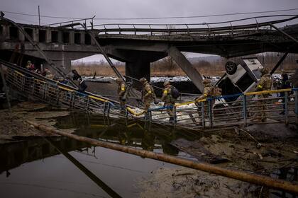 Soldados ucranianos cruzan un puente destruido, en las afueras de Kiev. Rusia renovó su asalto a la segunda ciudad más grande de Ucrania en un ataque que iluminó el horizonte con bolas de fuego sobre áreas pobladas