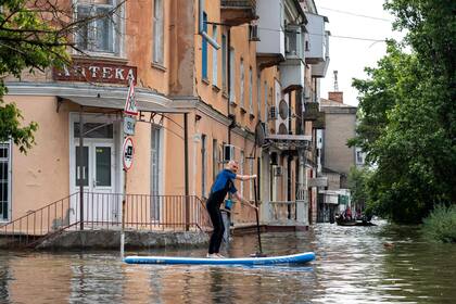 Un residente local navega en una tabla de surf durante una evacuación de un área inundada en Kherson el 8 de junio de 2023, luego de los daños sufridos en la represa de la central hidroeléctrica Kakhovka