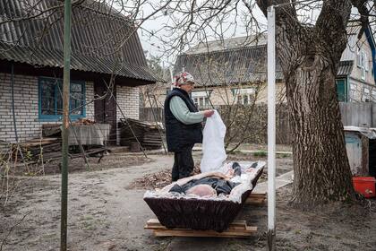Klavdia Samforskyi, de 79 años, extiende un cordón blanco para cubrir a su esposo Andriy, quien murió a la edad de 87 años a causa de una enfermedad. La mujer había enterrado a su esposo temporalmente en el fondo e su casa debido a los bombardeos en la ciudad de Bucha