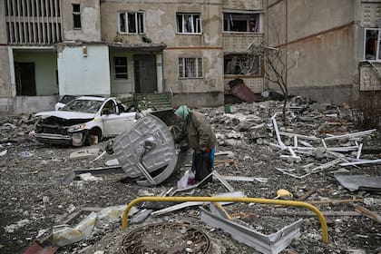 Una anciana revuelve la basura en medio de los escombros de un edificio que fue atacado con misiles rusos