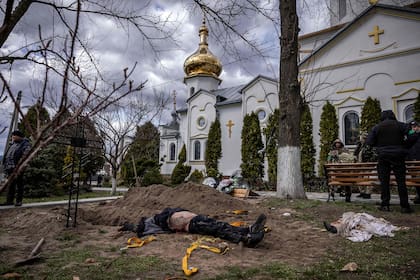 Una fotografía tomada el 12 de abril de 2022 muestra el cuerpo exhumado del alcalde de Gostomel, Yuriy Prylypko, quien fue enterrado cerca de una iglesia en el pueblo de Gostomel, región de Kyiv.  Prylypko, de 62 años, fue asesinado el 7 de marzo después de que las fuerzas rusas irrumpieran en la ciudad de Kyiv que administraba. El consejo municipal dijo que fue asesinado a tiros mientras "repartía pan a los hambrientos y medicinas a los enfermos".