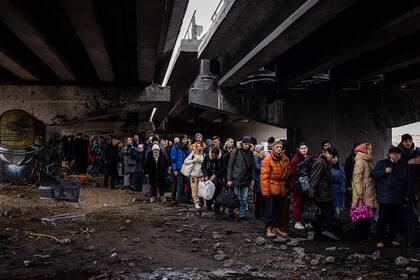 Miles  de personas que huyen de sus hogares tras los bombardeos rusos intentan cruzar un río bajo un puente que fue destruido en un ataque

