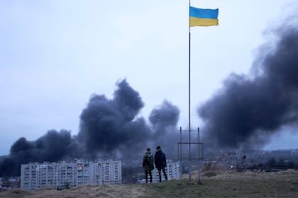 Las personas se paran frente a una bandera nacional ucraniana que ondea mientras observan el humo oscuro y las llamas que se elevan de un incendio luego de un ataque aéreo en la ciudad de Lviv, en el oeste de Ucrania
