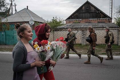 Soldados ucranianos pasan mientras Polina (derecha), de 15 años, y su prima Nastya, de 16, llevan flores a la madre de Polina para celebrar su cumpleaños mientras se escuchan fuertes bombardeos a lo lejos en Raihorodok, al este de Ucrania