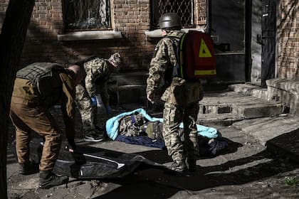 Miembros del servicio militar de emergencia retiran el cuerpo de un militar ucraniano muerto en el área de un instituto de investigación, parte de la Academia Nacional de Ciencias de Ucrania, después de un ataque, en el noroeste de Kiev, el 22 de marzo de 2022